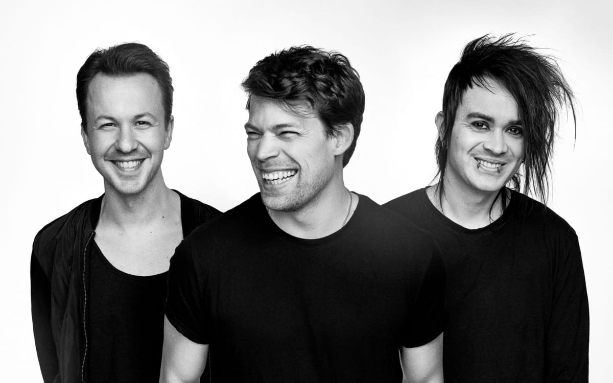 Black and white promotional photo of the Swedish band Dirty Loops, featuring the three members standing side by side, smiling.